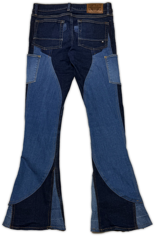 A pair of denim jeans with a unique patchwork design featuring dark blue and medium blue denim panels, photographed flat against a white background.