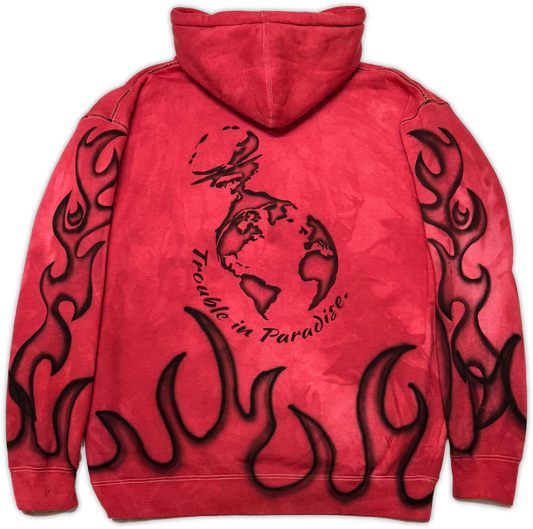 A red hooded sweatshirt shown from the back, featuring a black graphic of a globe with a rabbit and the text 'trouble in Paradise' across the center, with black flame motifs printed along the sleeves and lower back.