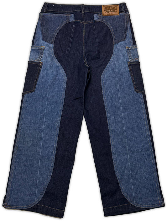 A pair of patchwork denim work pants shown from the back, featuring dark indigo and medium blue denim panels, with a brown leather brand patch on the back waistband.
