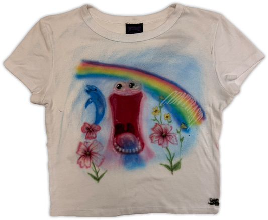A white-colored short-sleeve t-shirt featuring a colorful spray-painted graphic of a smiling open mouth, a blue dolphin, pink flowers, and a rainbow on the front.