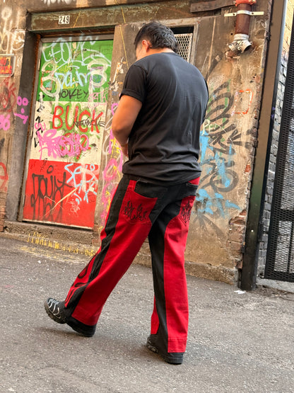 A man wearing red and black athletic pants and a black t-shirt walks past a graffiti-covered alleyway.