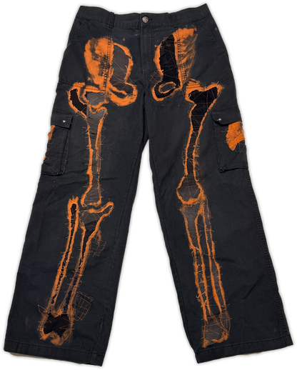 Black cargo pants featuring a prominent orange bone x-ray style graphic printed across the front, displayed flat against a white background.