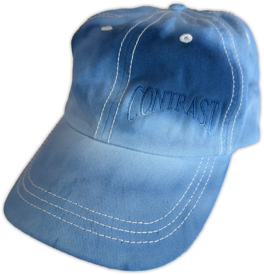 A light blue baseball cap with white contrast stitching and 'CONTRAST' embroidered in blue on the front, shown against a plain white background.