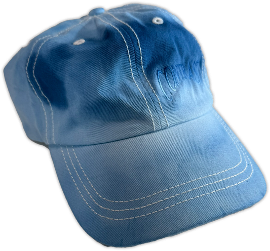 A blue denim baseball cap with white contrast stitching and embroidered text on the side, shown against a plain white background.