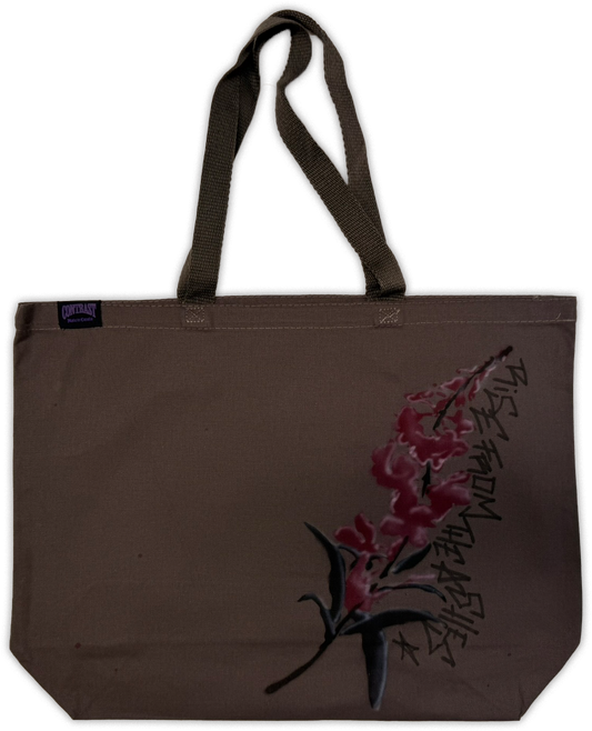 A brown canvas tote bag with dark brown webbed handles, featuring a graphic print of pink flowers and black calligraphy on the lower right side.