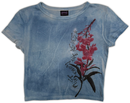 A short-sleeve crewneck t-shirt in a blue tie-dye wash, featuring a graphic print of a pink flower with green leaves and black script text on the front.