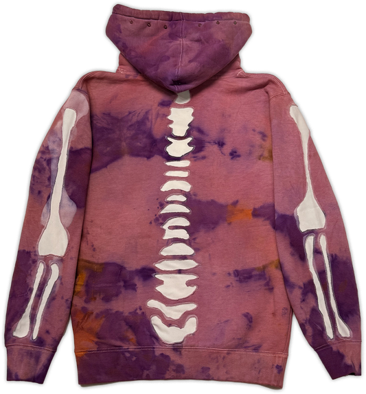 A purple and pink tie-dye hoodie with a white skeleton spine graphic running down the center back, flanked by white skeleton arm and leg graphics on both sleeves, shown against a plain white background.