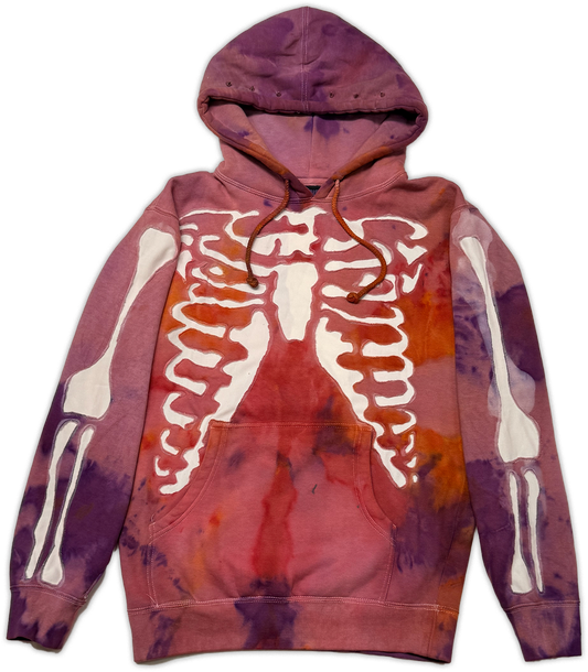 A purple and red tie-dye hoodie featuring a white cut out patch of a skeleton rib cage graphic on the chest and white bone cut out patched on both sleeves.