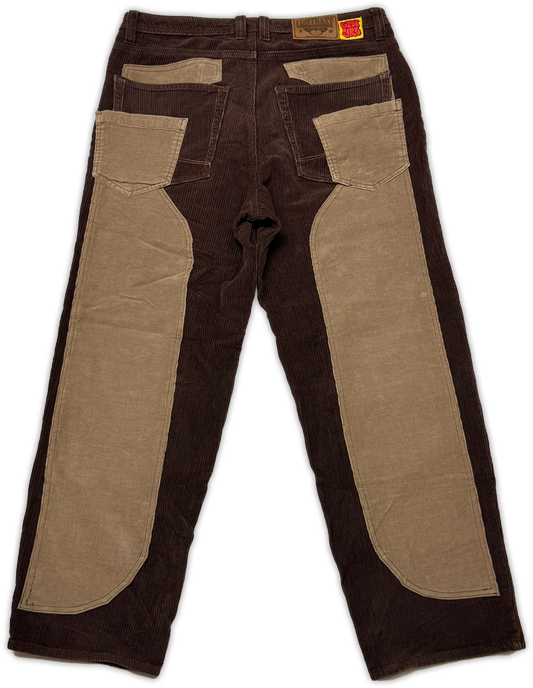 A pair of dark brown corduroy pants with contrasting tan canvas knee patches and back pocket flaps, shown flat against a white background.