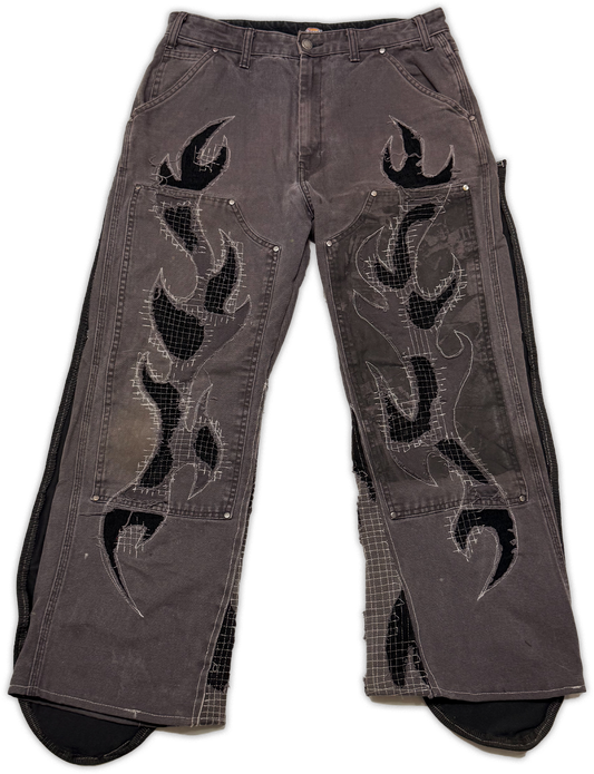 A pair of faded dark gray denim jeans with black flame applique patches and silver studs on the front, shown against a plain white background.