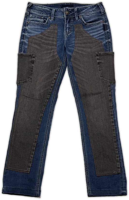 A pair of blue denim jeans with large dark gray fabric panels on the front of the thighs and side cargo pockets, shown flat against a white background.