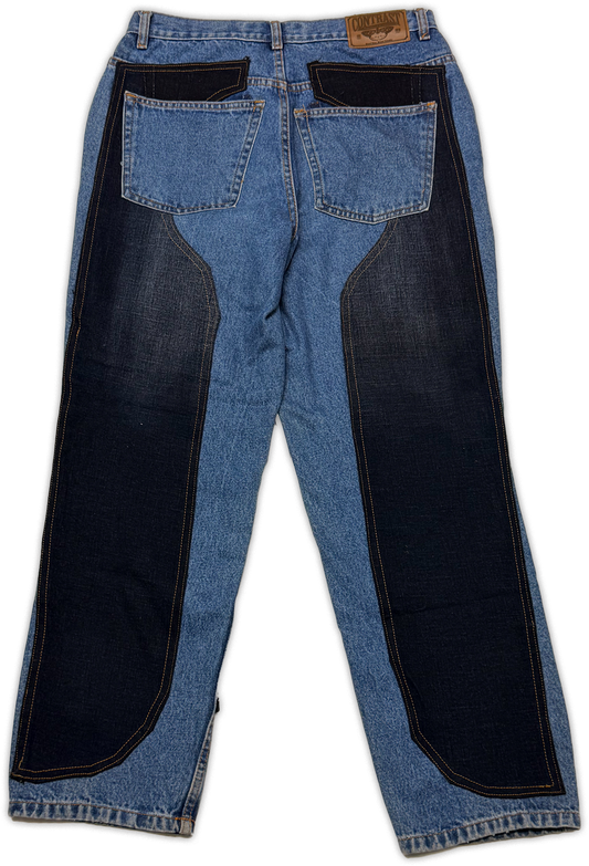 A pair of blue denim jeans shown from the back, featuring large dark navy blue patch panels on the outer sides of the legs and dark brown leather patch reading “contrast”. 
