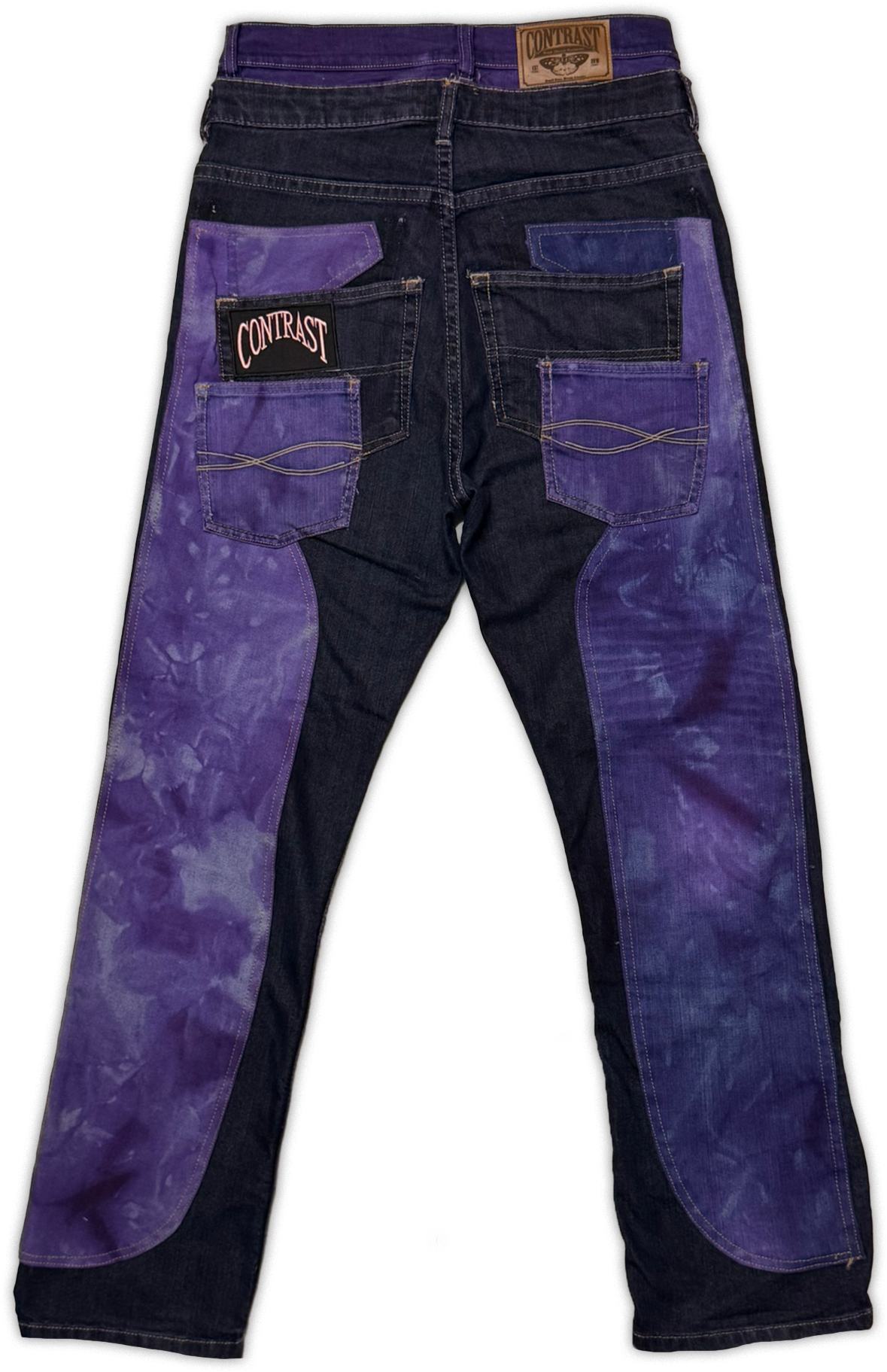 Back view of a pair of jeans with dark navy denim and prominent purple tie-dye panels on the back pockets and legs. The back pocket features a black patch with the brand name 'Contrast' in pink.