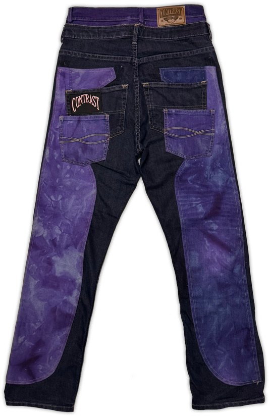 Back view of a pair of jeans with dark navy denim and prominent purple tie-dye panels on the back pockets and legs. The back pocket features a black patch with the brand name 'Contrast' in pink.