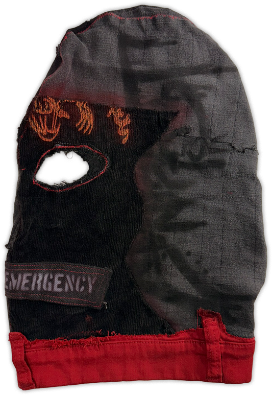 A distressed black fabric balaclava or face covering with a large eye opening, featuring orange embroidered skull-like graphics, a gray 'EMERGENCY' patch, and a bright red frayed trim along the bottom edge.