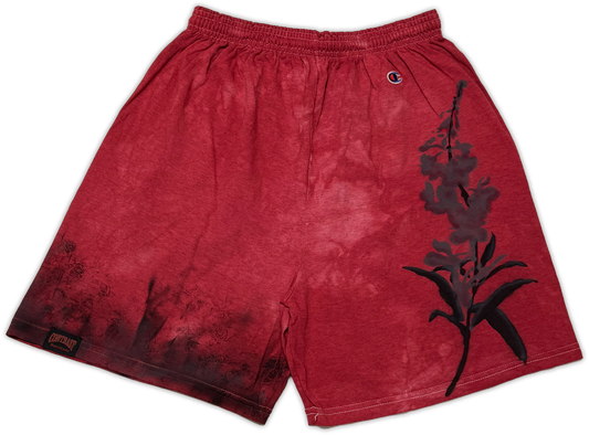 Red acid-wash Champion athletic shorts featuring a black floral graphic on the right leg and a small Champion logo near the waistband.