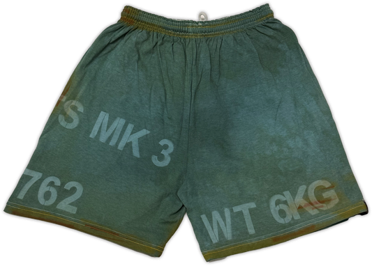 A pair of faded olive green canvas shorts with white printed text reading 'S MK 3', '762', and 'WT 6KG' on a white background.
