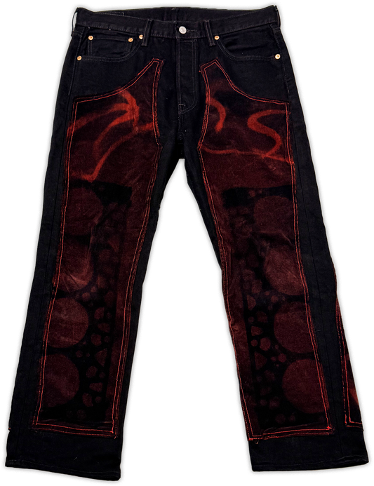 Black denim jeans with a dark red and black abstract graphic print on the front thigh panels and red contrast stitching, shown flat against a white background.