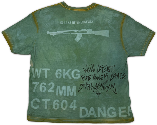 A green distressed short-sleeve t-shirt with military-style graphics and text, including a rifle silhouette, 'IN CASE OF EMERGENCY' at the neck, and 'DANGER' with handwritten-style text on the back.