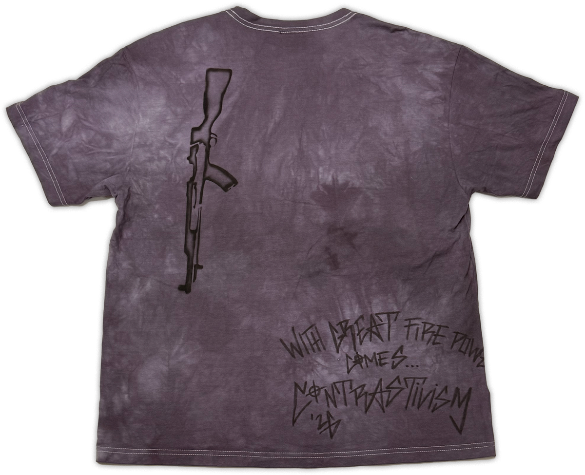 A short-sleeve t-shirt with a dark purple and gray mineral-wash finish, featuring a black line-art graphic of an assault rifle on the upper left and stylized black text on the lower right that reads 'WITH great power comes.. contrast”.