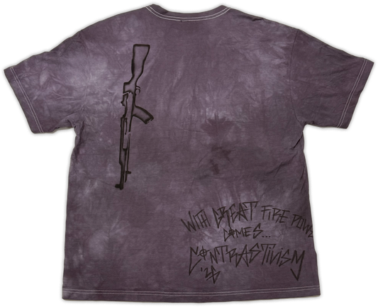 A short-sleeve t-shirt with a dark purple and gray mineral-wash finish, featuring a black line-art graphic of an assault rifle on the upper left and stylized black text on the lower right that reads 'WITH great power comes.. contrast”.