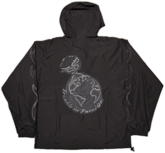 A black hooded windbreaker jacket shown flat against a white background, featuring a large tonal graphic on the back with a globe being nuked, and the text 'trouble in paradise' wrapped around it.
