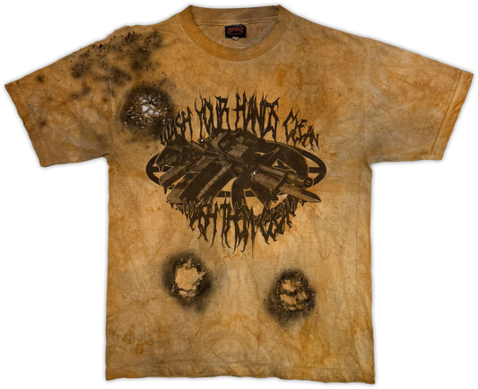 A short-sleeve graphic t-shirt with a distressed, acid-washed tan and brown color scheme. The shirt features a central black graphic of a rifle with the text 'WASH YOUR HANDs clean' and 'wash your hands' in a stylized font, along with three simulated bullet holes on the front.
