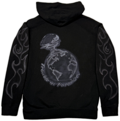 Black pullover hoodie shown from the back, featuring a large gray graphic of a globe with the words 'trouble in paradise' curved around it, plus gray flame-like sleeve prints.